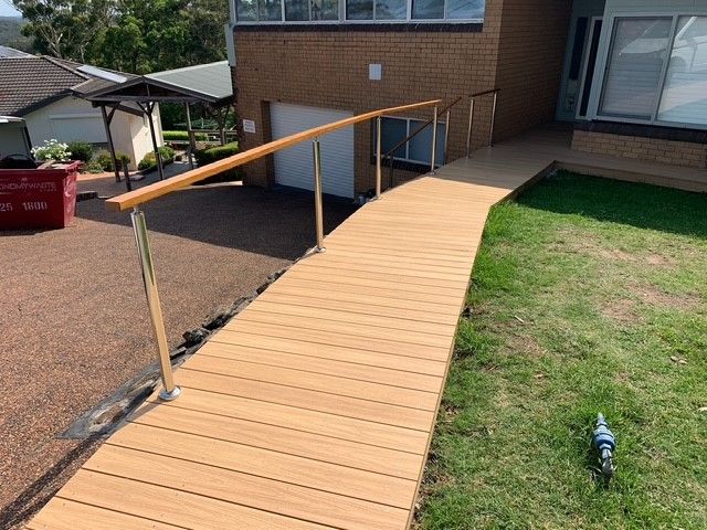 A wooden ramp leading to a house with a stainless steel railing.