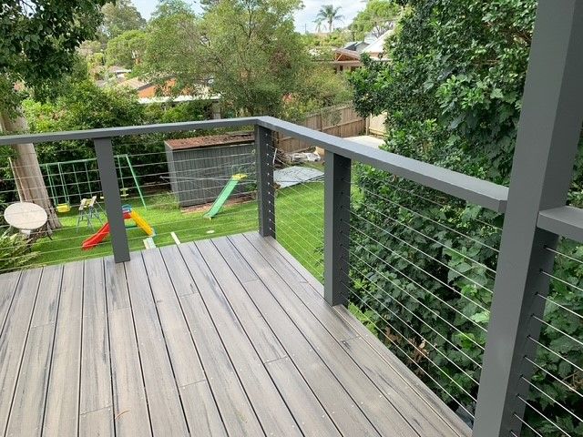 A wooden deck with a metal railing and a swing set in the background.