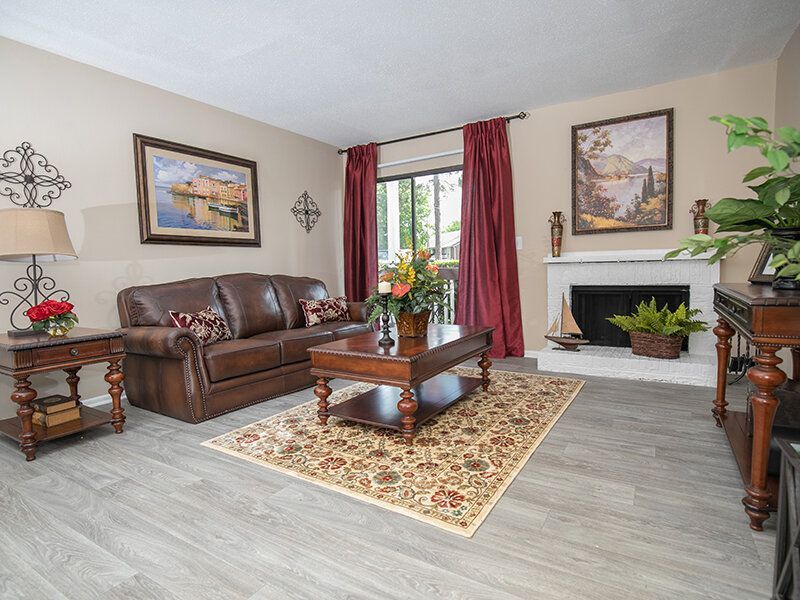 Living room with brown leather sofa, rug, fireplace, artwork, and red curtains.