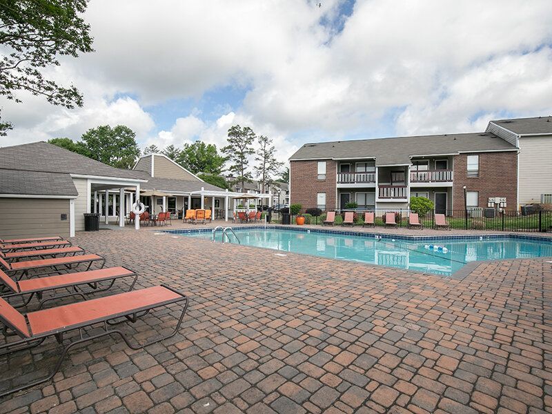 Outdoor apartment community pool with brick-paved pool deck and orange lounge chairs