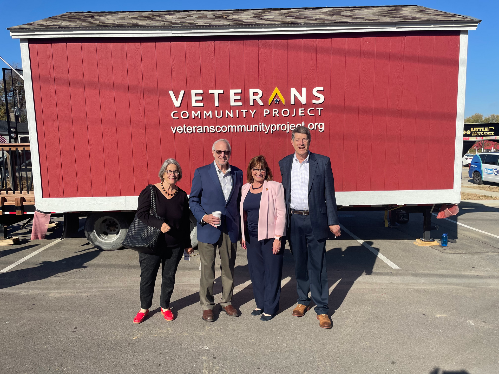 Joe Pereles and company are standing in front of a red trailer that says veterans community project.