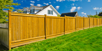 A wooden fence surrounds a lush green lawn in front of a house.