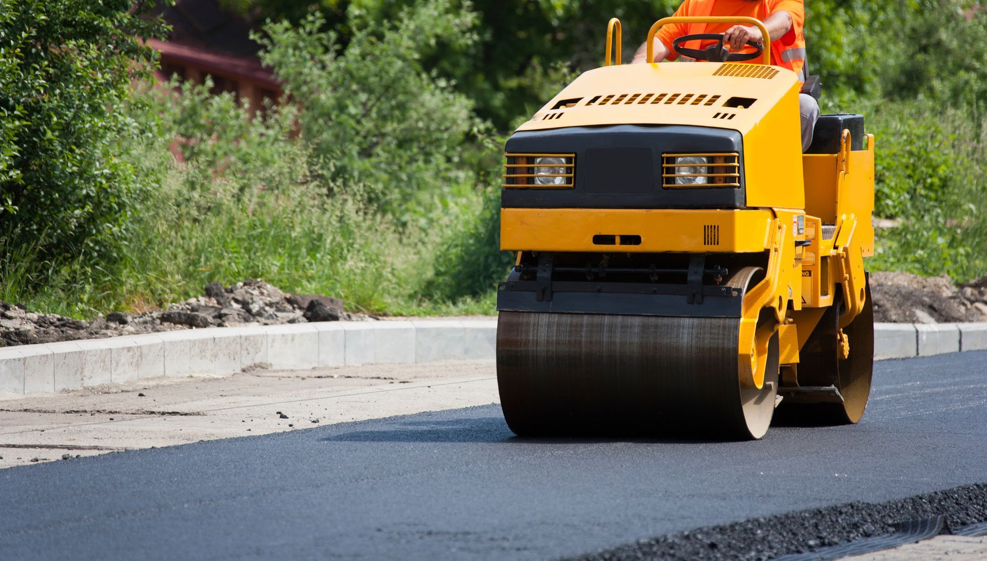 Asphalt paving contractor operates a road roller to smooth asphalt on a road under construction.