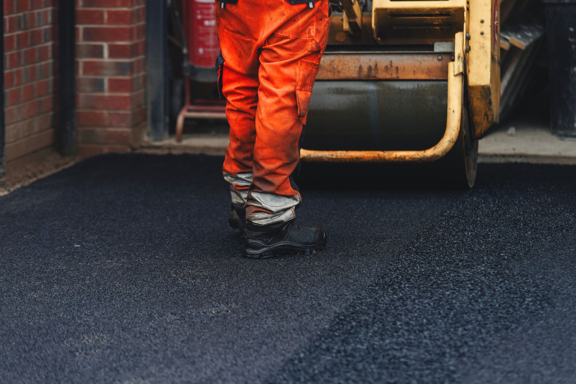 Construction worker operating machinery on freshly laid asphalt in a parking lot project.