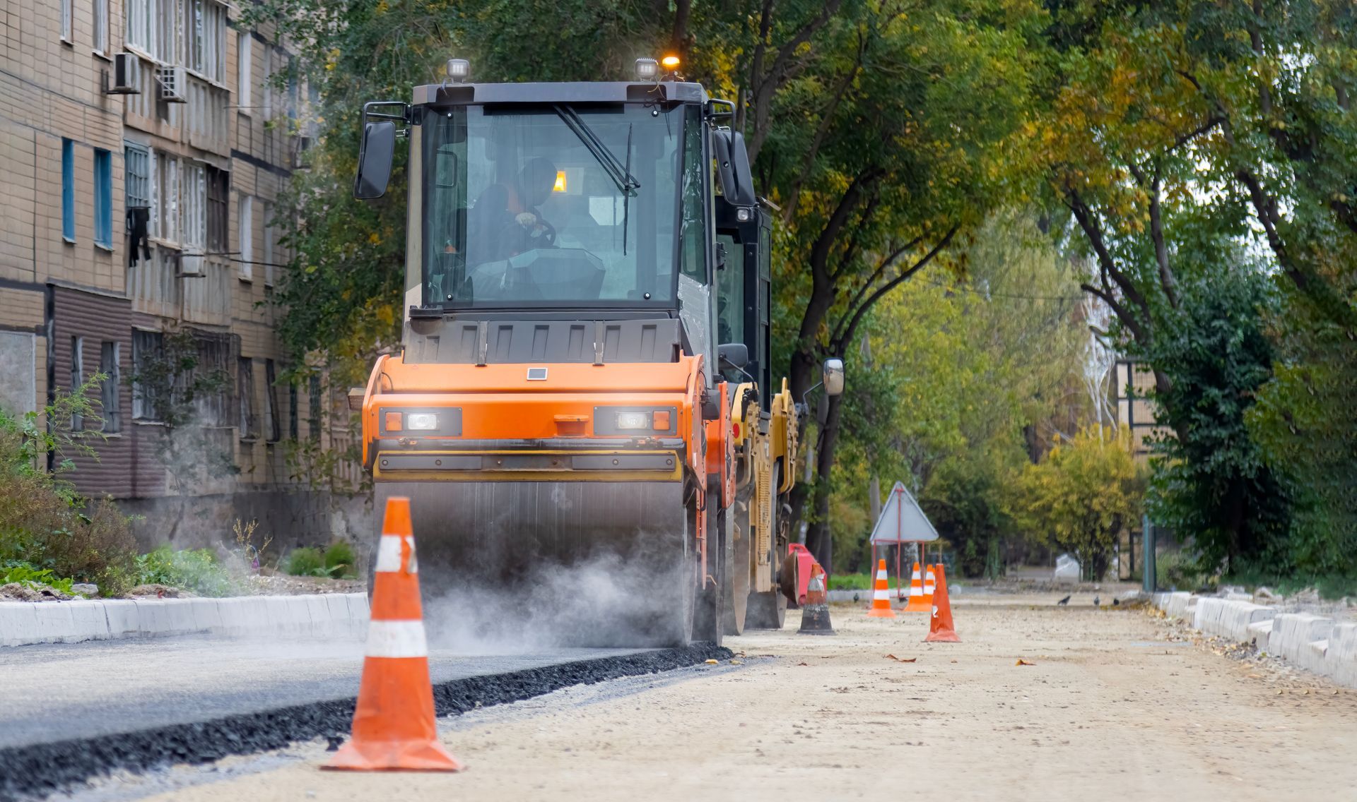 Asphalt paving contractor using a spreader to lay the first layer of asphalt on a city street.