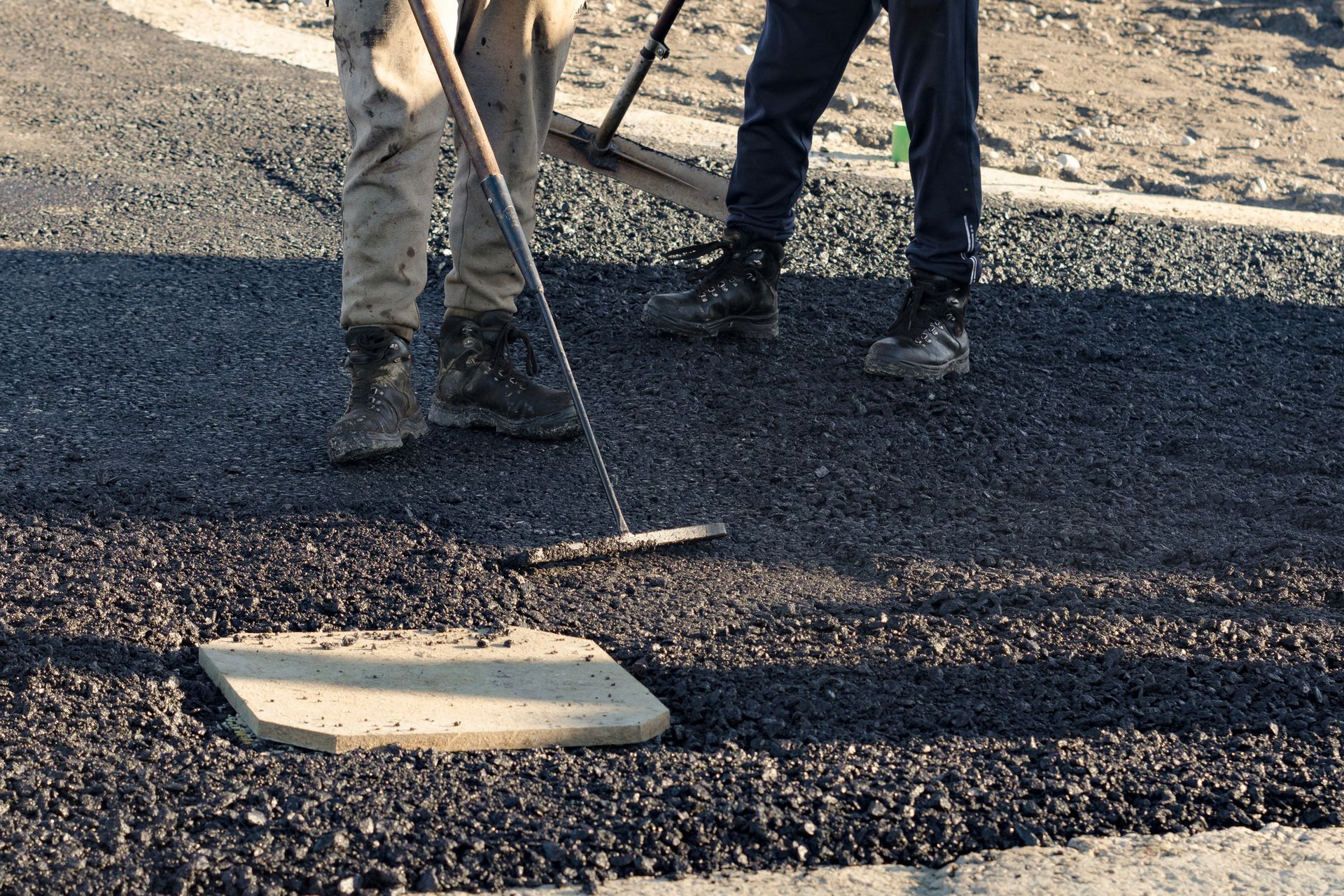 Construction workers in high-visibility gear are applyin gfresh hot asphalt.