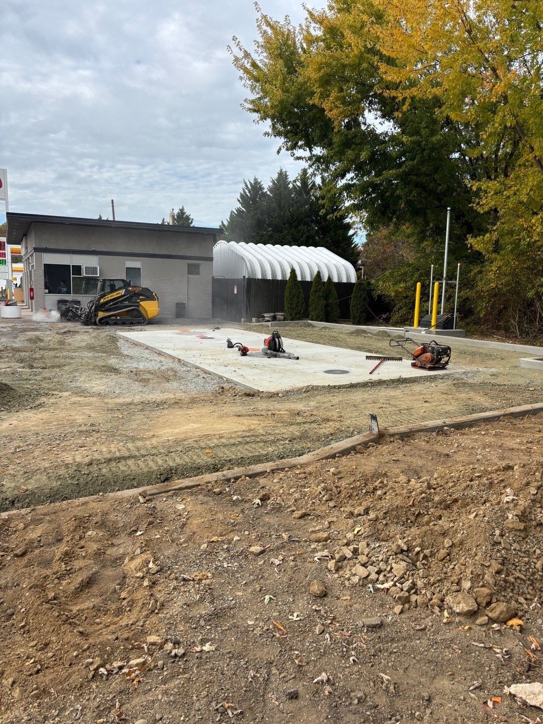 Outdoor construction site with a concrete slab, workers, a gray building, and a white canopy under cloudy skies