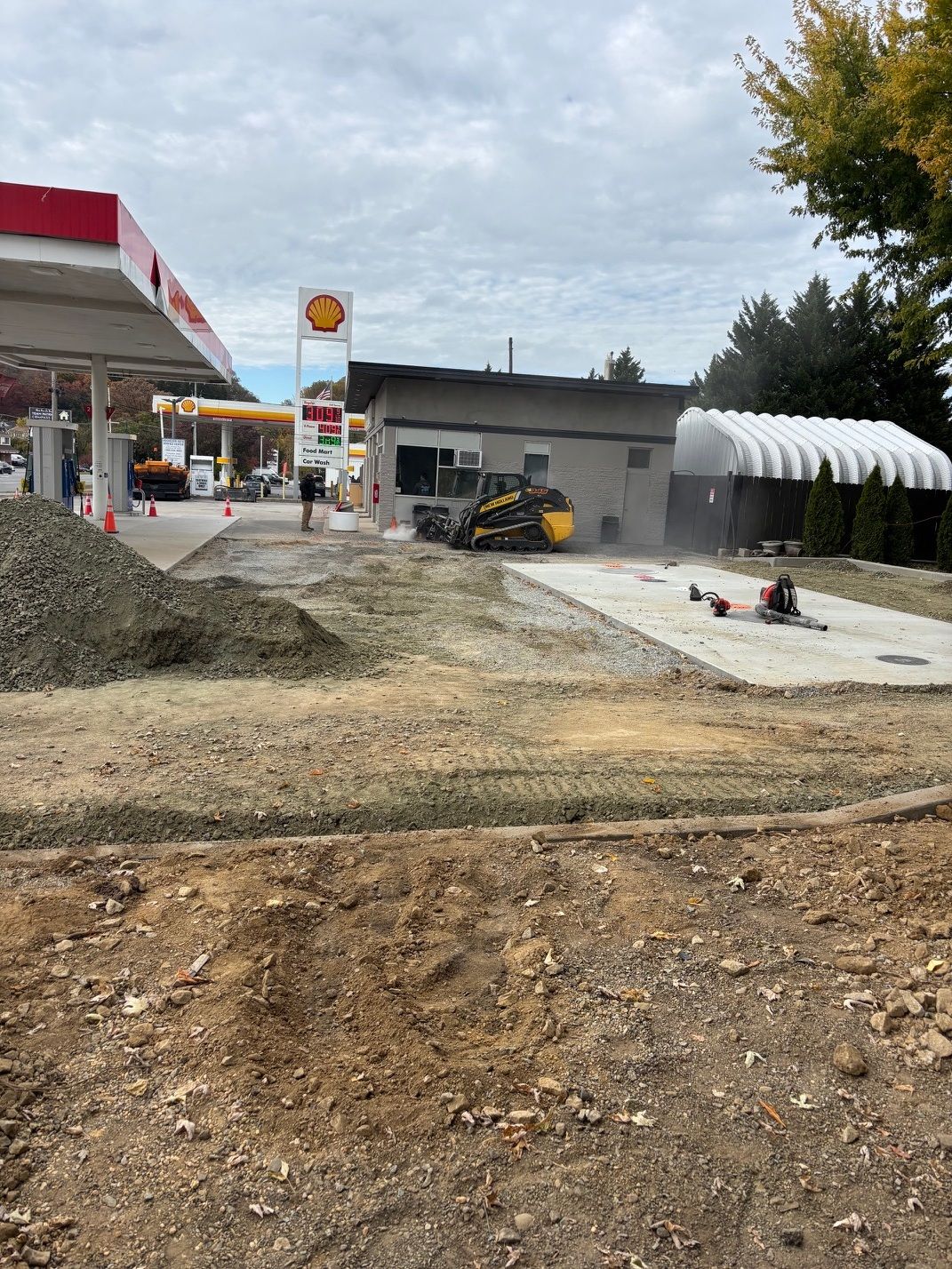 Shell gas station under construction, with visible excavation, gravel piles, and a small building.