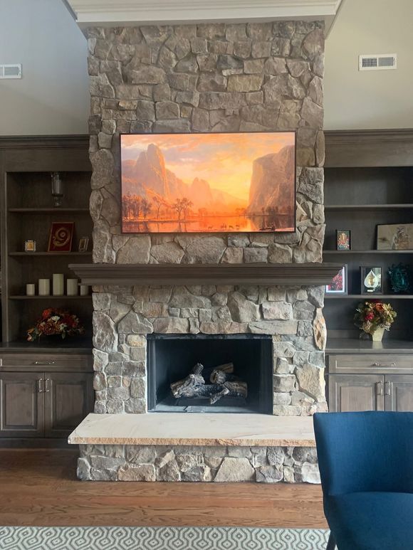 Stone fireplace with built-in shelves and a glowing wall-mounted TV above the mantel.