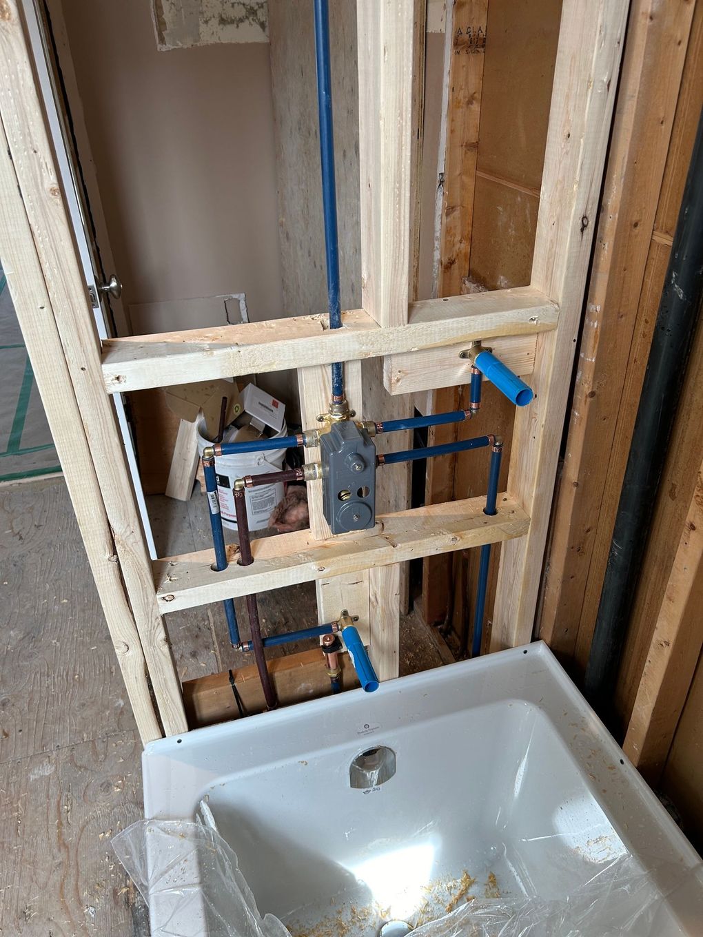 Plomberie brute pour une baignoire, montrant des tuyaux PEX bleus, une vanne et la baignoire elle-même dans un mur encadré.