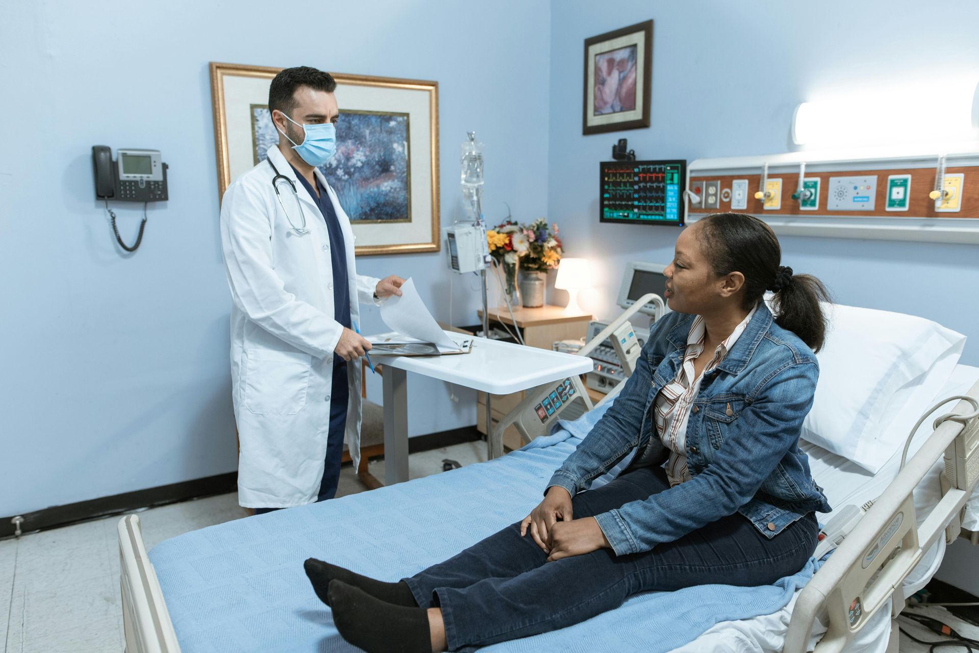 A woman sitting on a hospital examination bed being examined by a doctor
