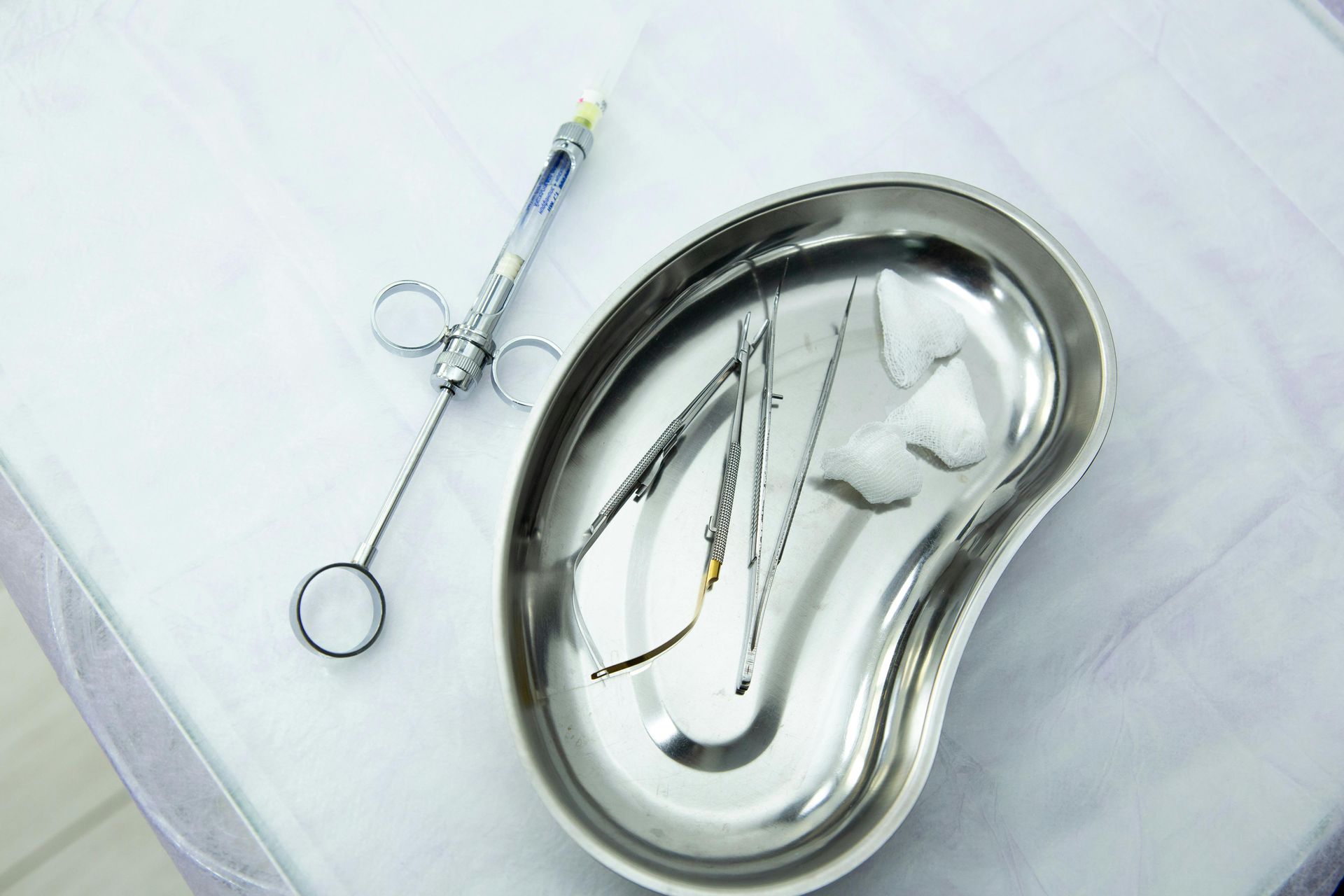 A stainless-steel kidney pan containing neatly arranged medical tools used for renal care procedures