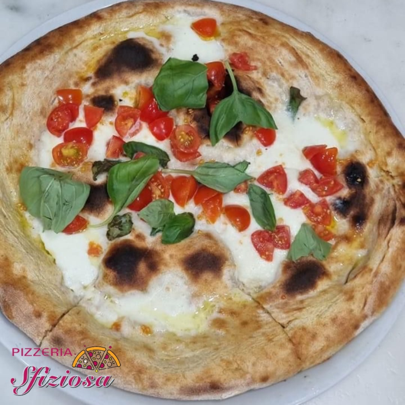 Pizza con mozzarella, pomodori e basilico su un piatto bianco.