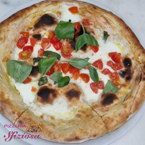 Pizza con mozzarella, pomodori e basilico su un piatto bianco.