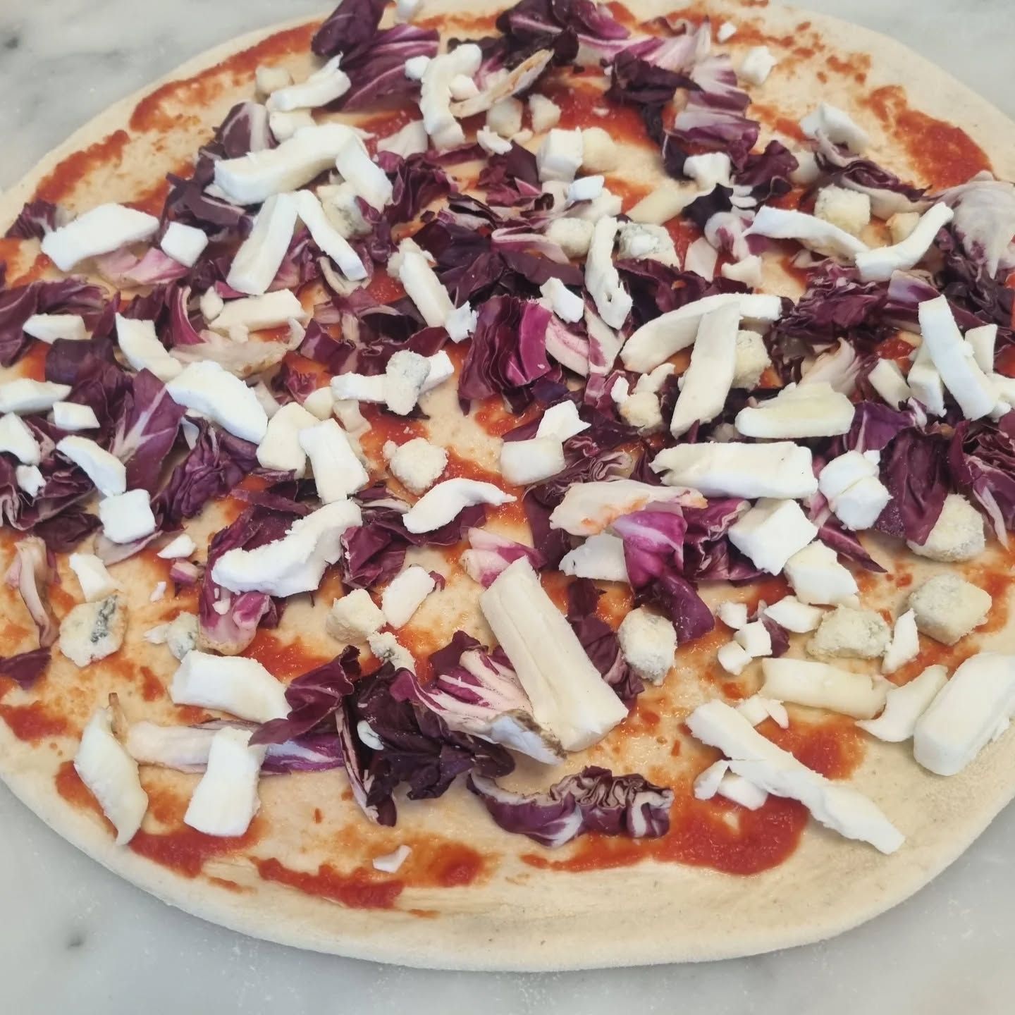 Pizza con radicchio rosso e formaggio bianco su una superficie bianca.