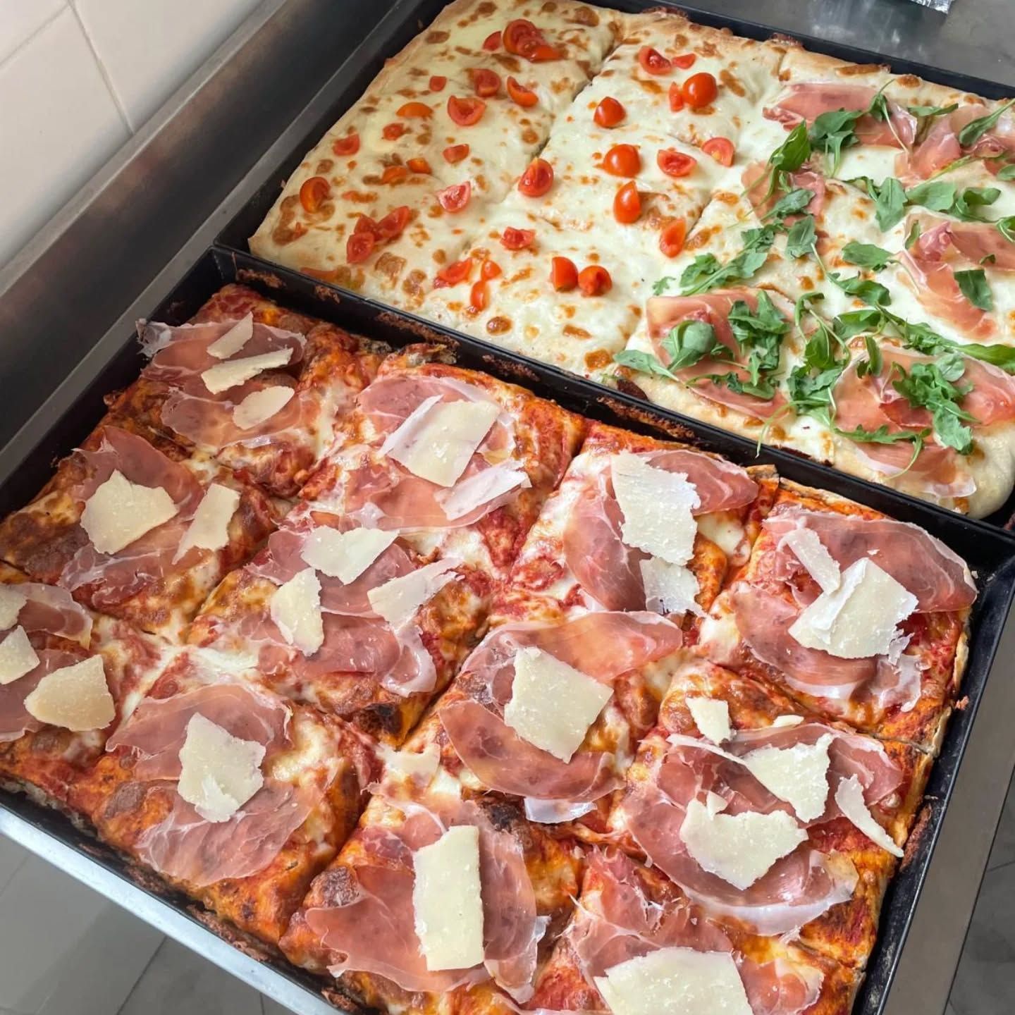 Pizze quadrate: pomodoro e formaggio, prosciutto e parmigiano, in una teglia da forno.