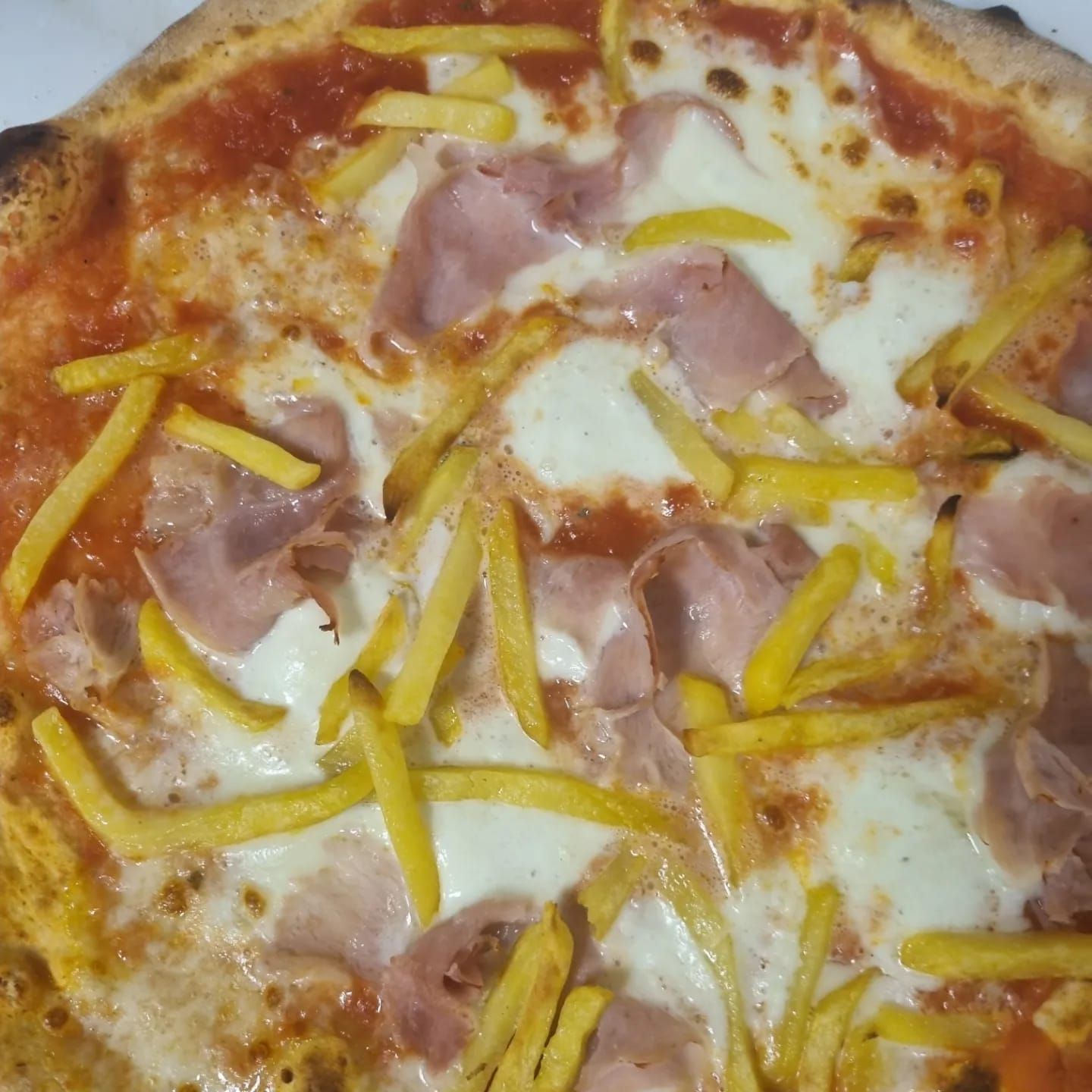 Pizza con prosciutto, mozzarella, salsa di pomodoro e patatine fritte.