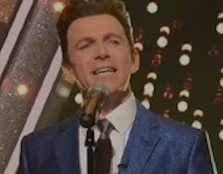 A man in a suit and tie is singing into a microphone.