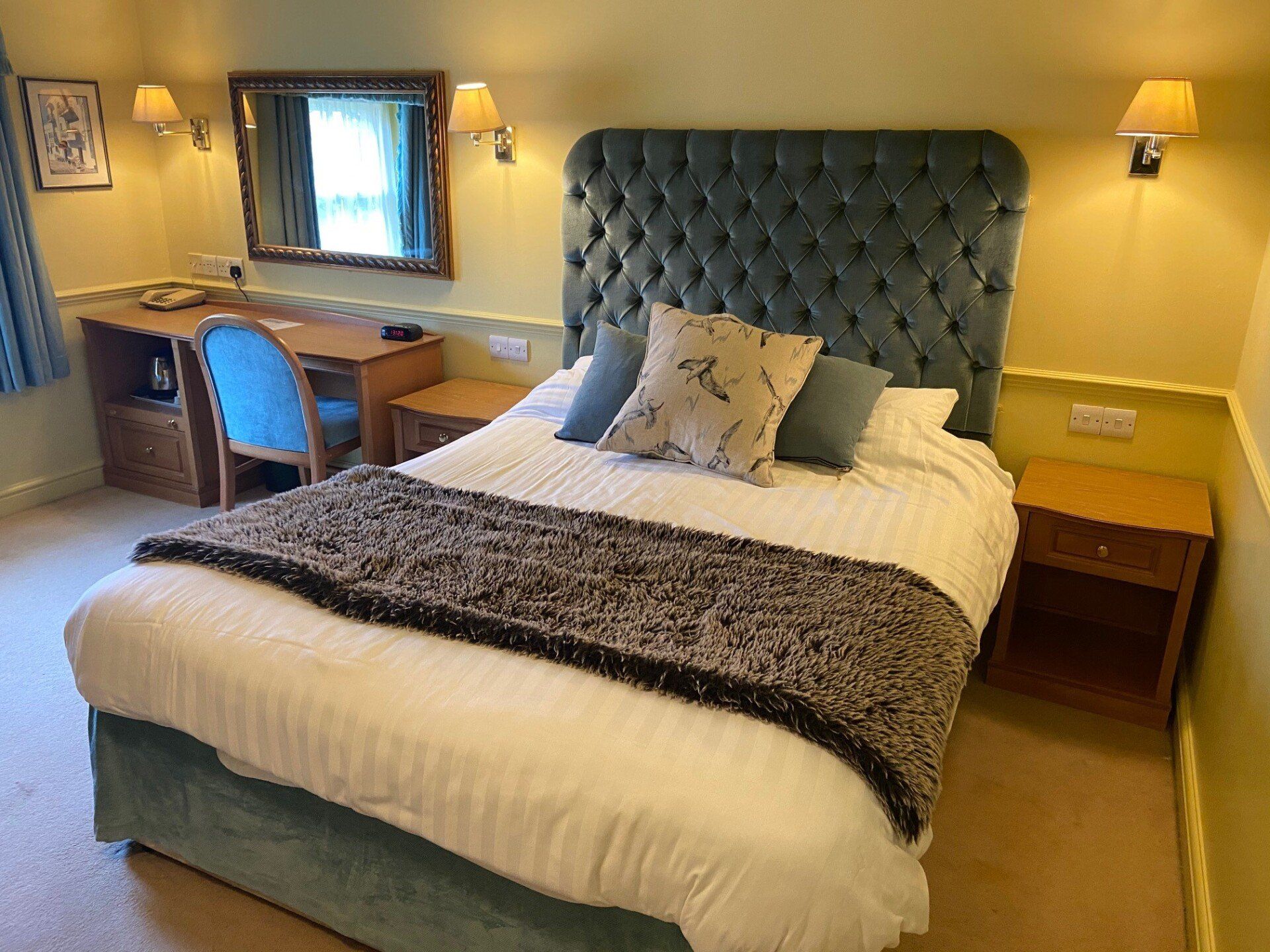 A hotel room with a bed , desk , nightstand and mirror.