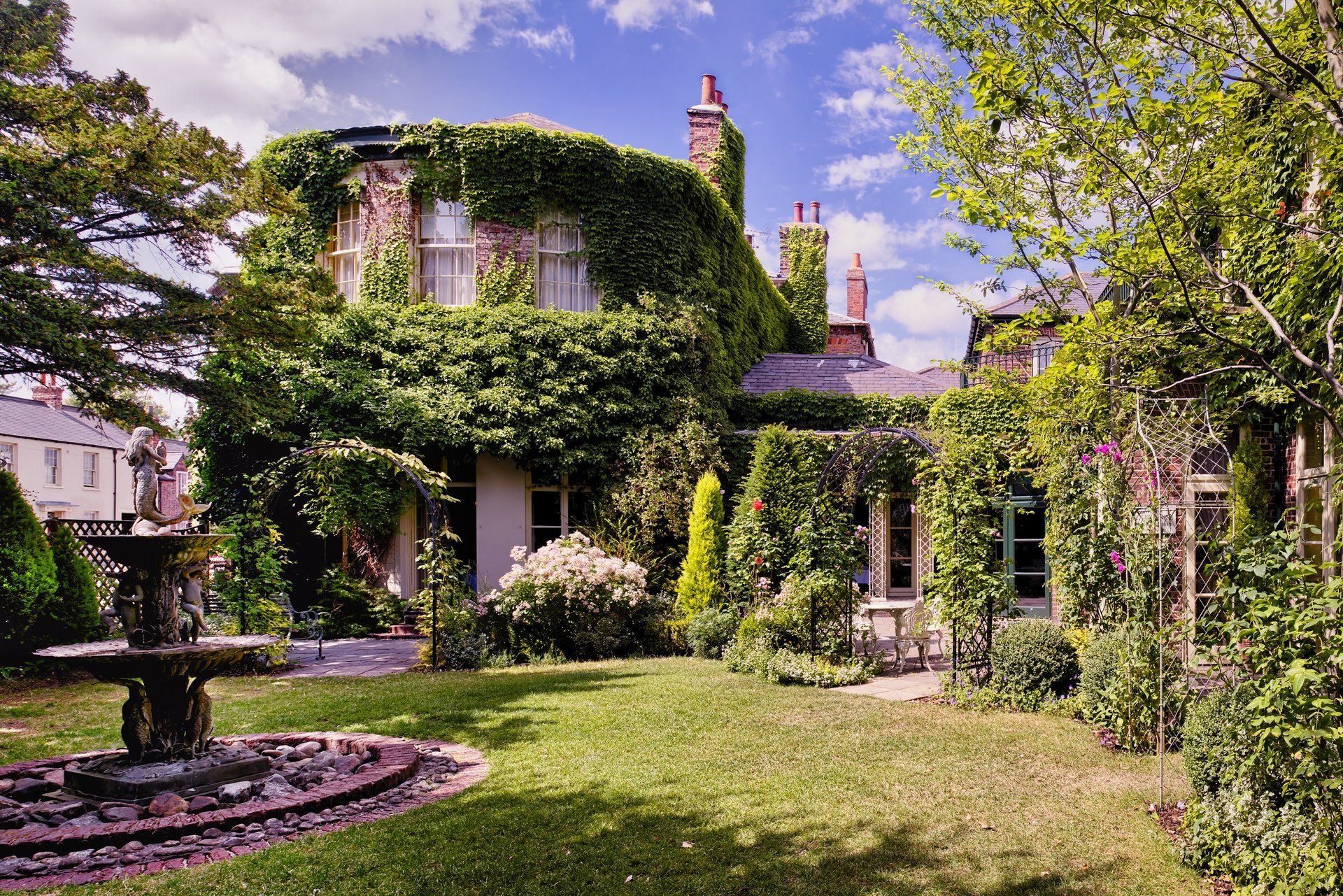 A large house with a fountain in front of it surrounded by trees and bushes.