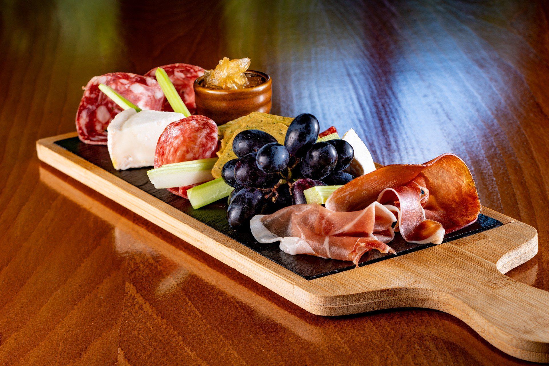 A wooden cutting board filled with meats and grapes on a wooden table.