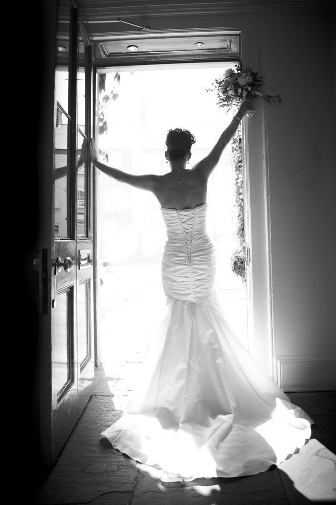 A bride in a wedding dress is standing in a doorway holding a bouquet of flowers.