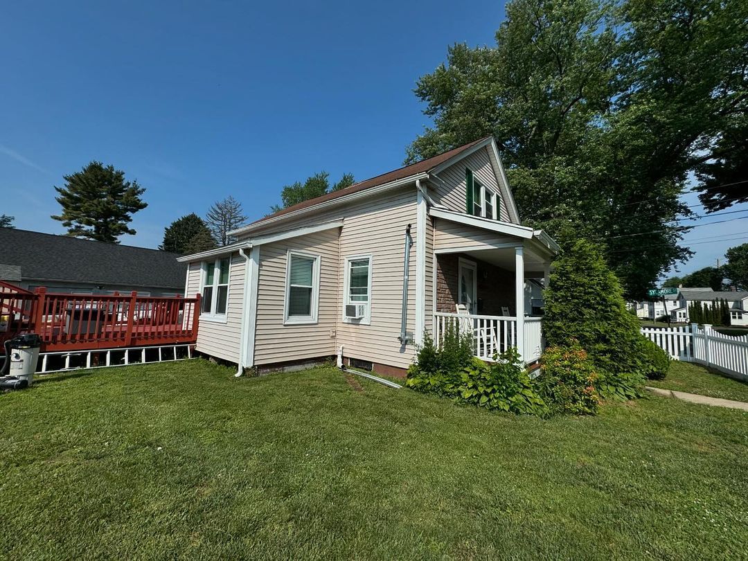 A small white house with a red deck in the backyard.