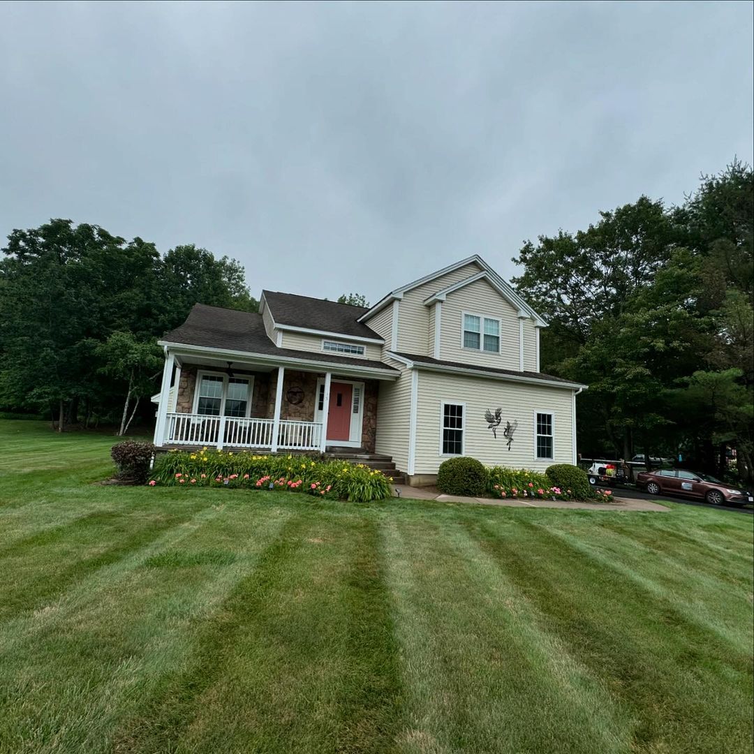 A white house with a porch sits in the middle of a lush green field