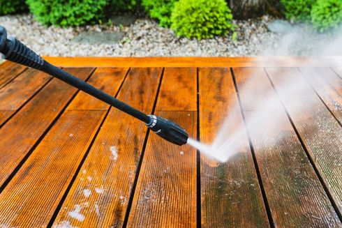 A person is using a high pressure washer to clean a wooden deck.