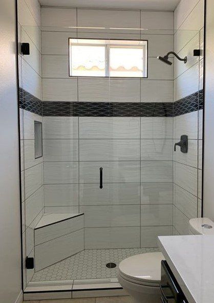A bathroom with a shower , toilet , sink and window.