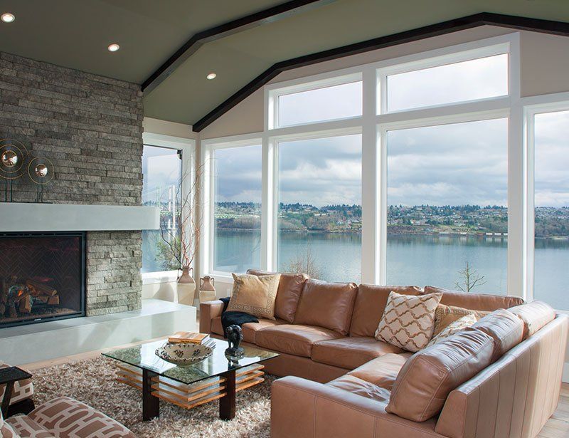 A living room with a couch , fireplace , and lots of windows overlooking a lake.
