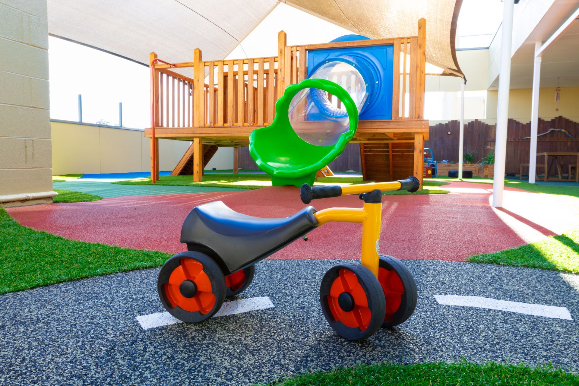 A toy tricycle is sitting on the ground in a playground.