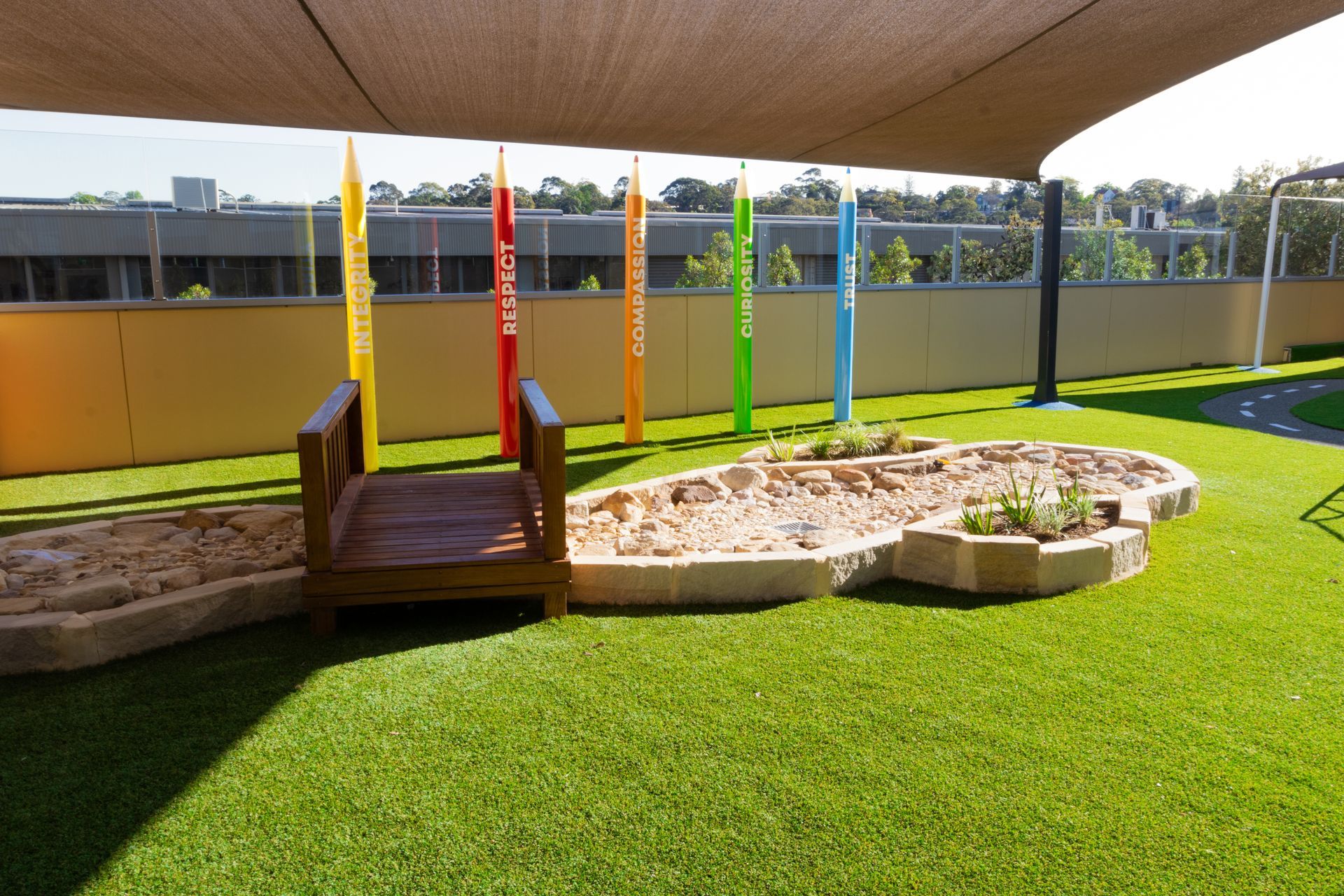 A playground with a bridge and a sandbox under an umbrella.