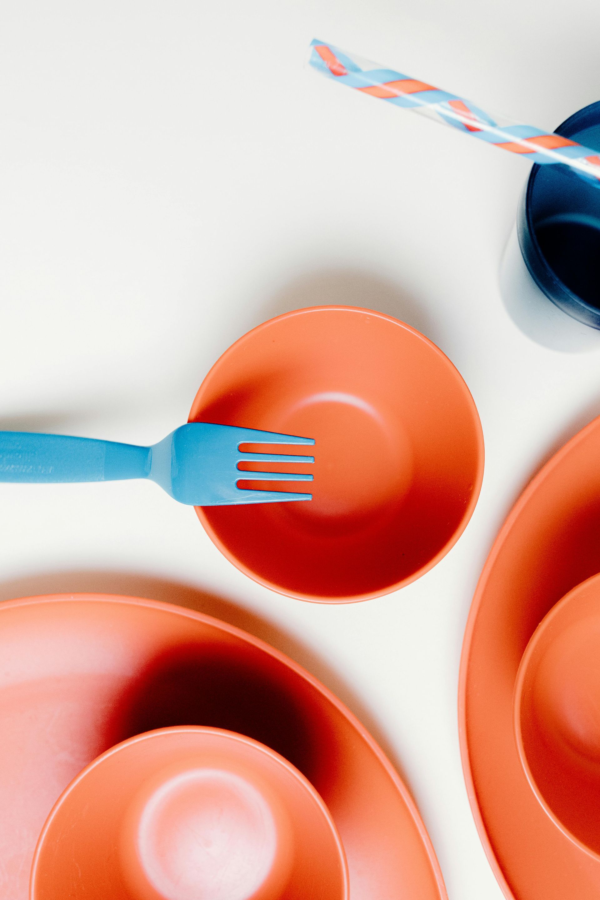 A blue fork is sitting on top of an orange bowl on a table.