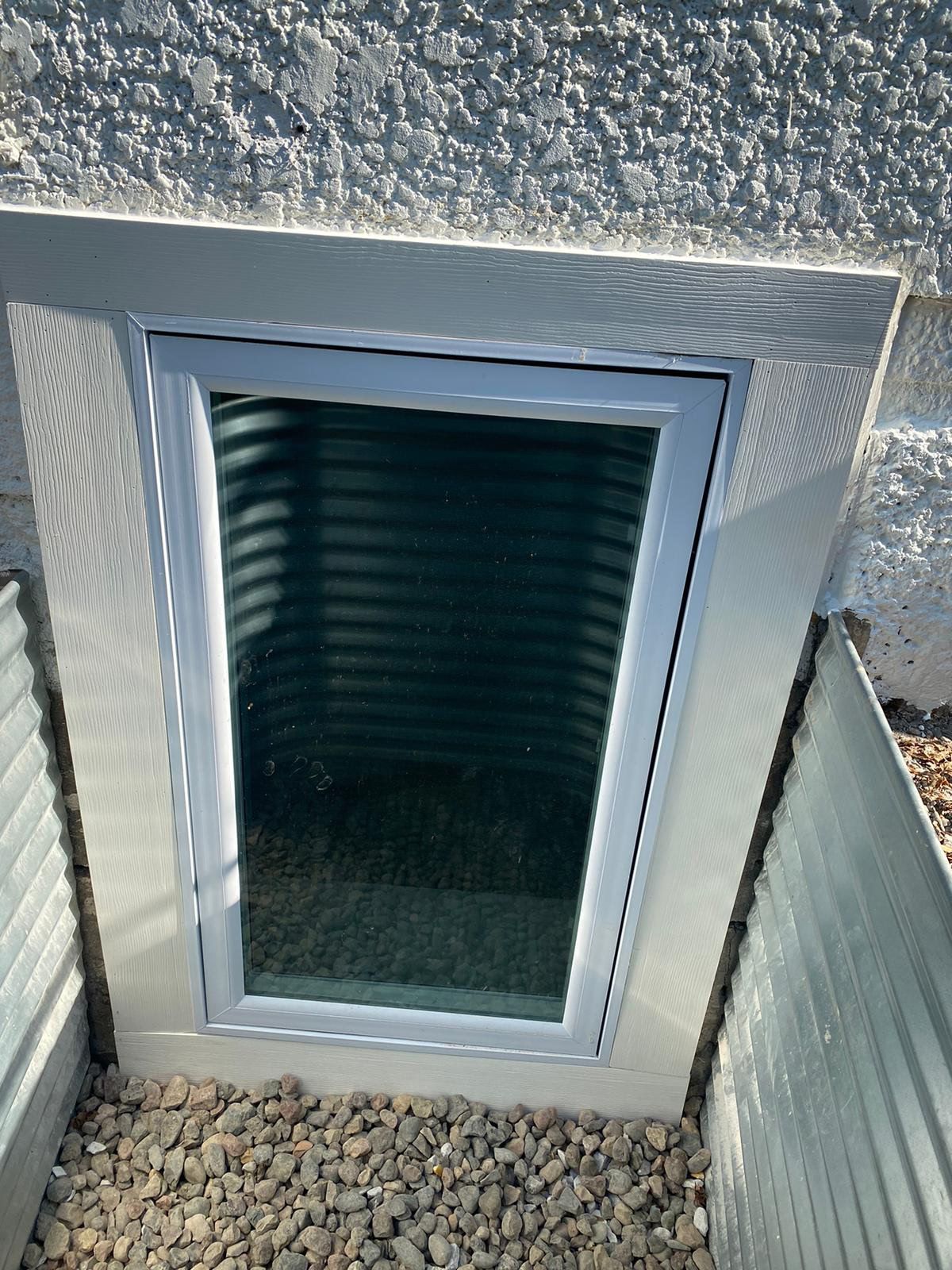 Window well with a rectangular window, surrounded by a white frame and gravel.
