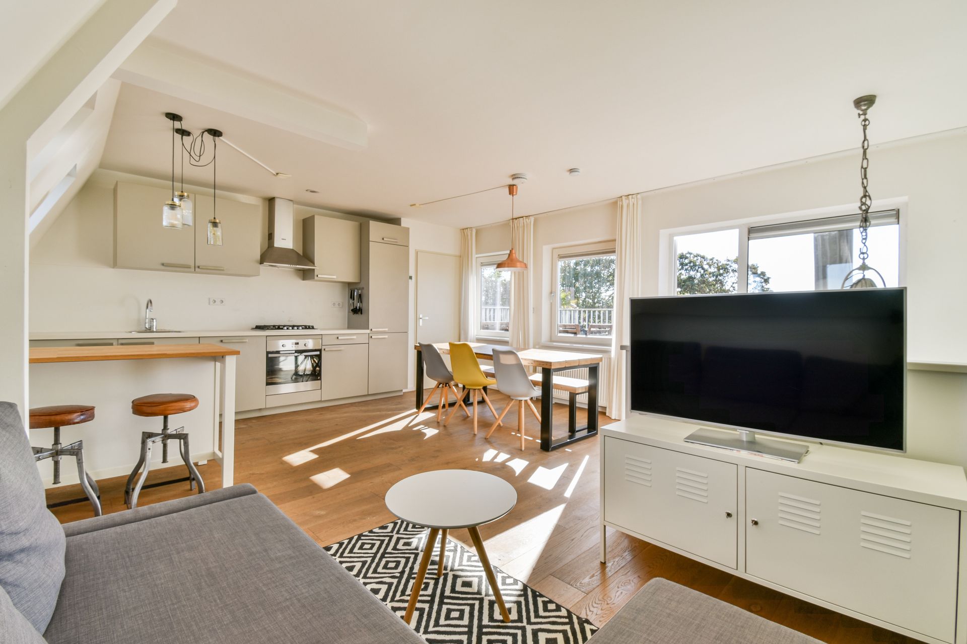 Open-plan living space with kitchen, dining table, and TV on a white cabinet.