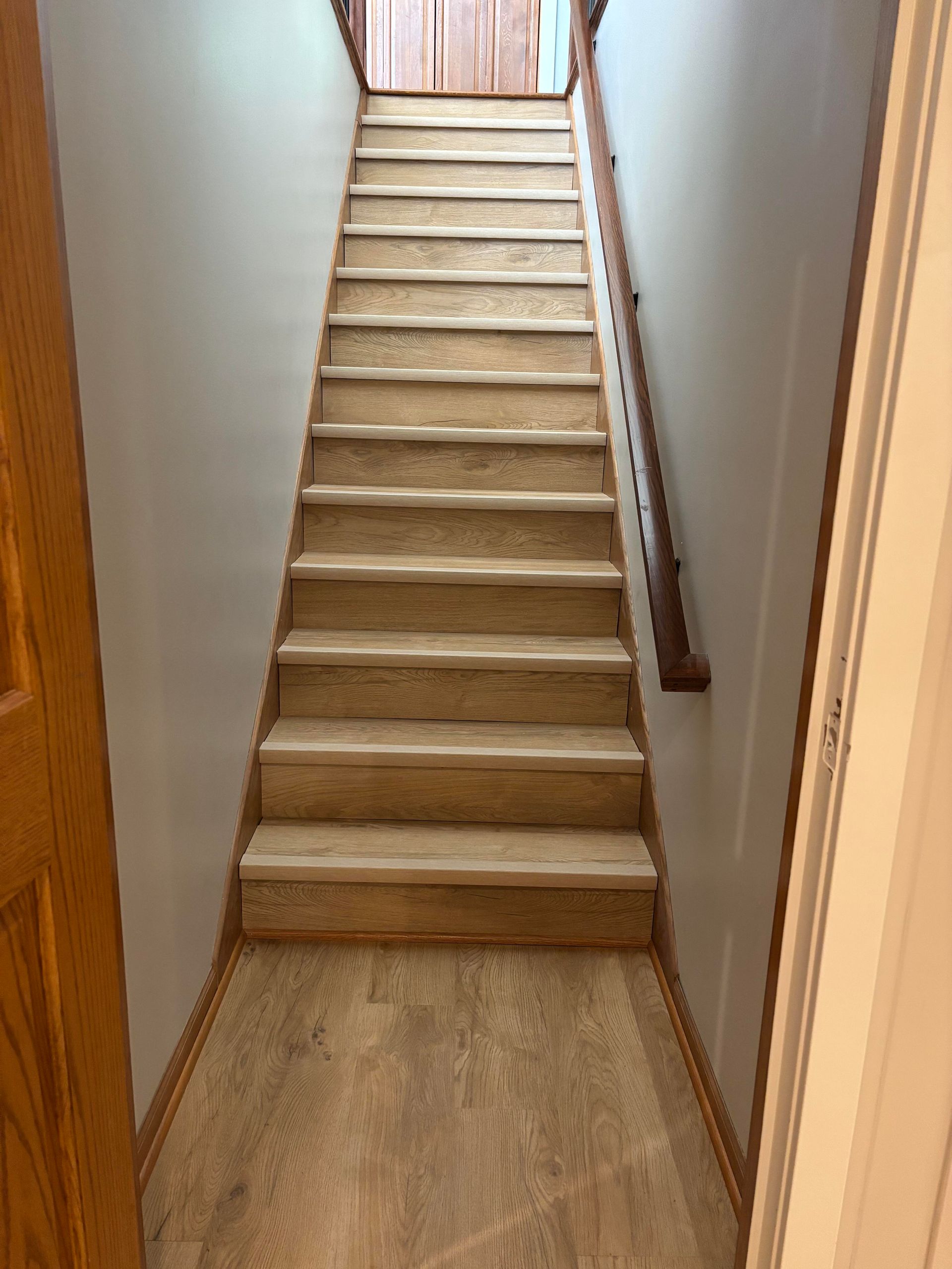 Staircase with light wood steps and handrail leading upwards between light gray walls.