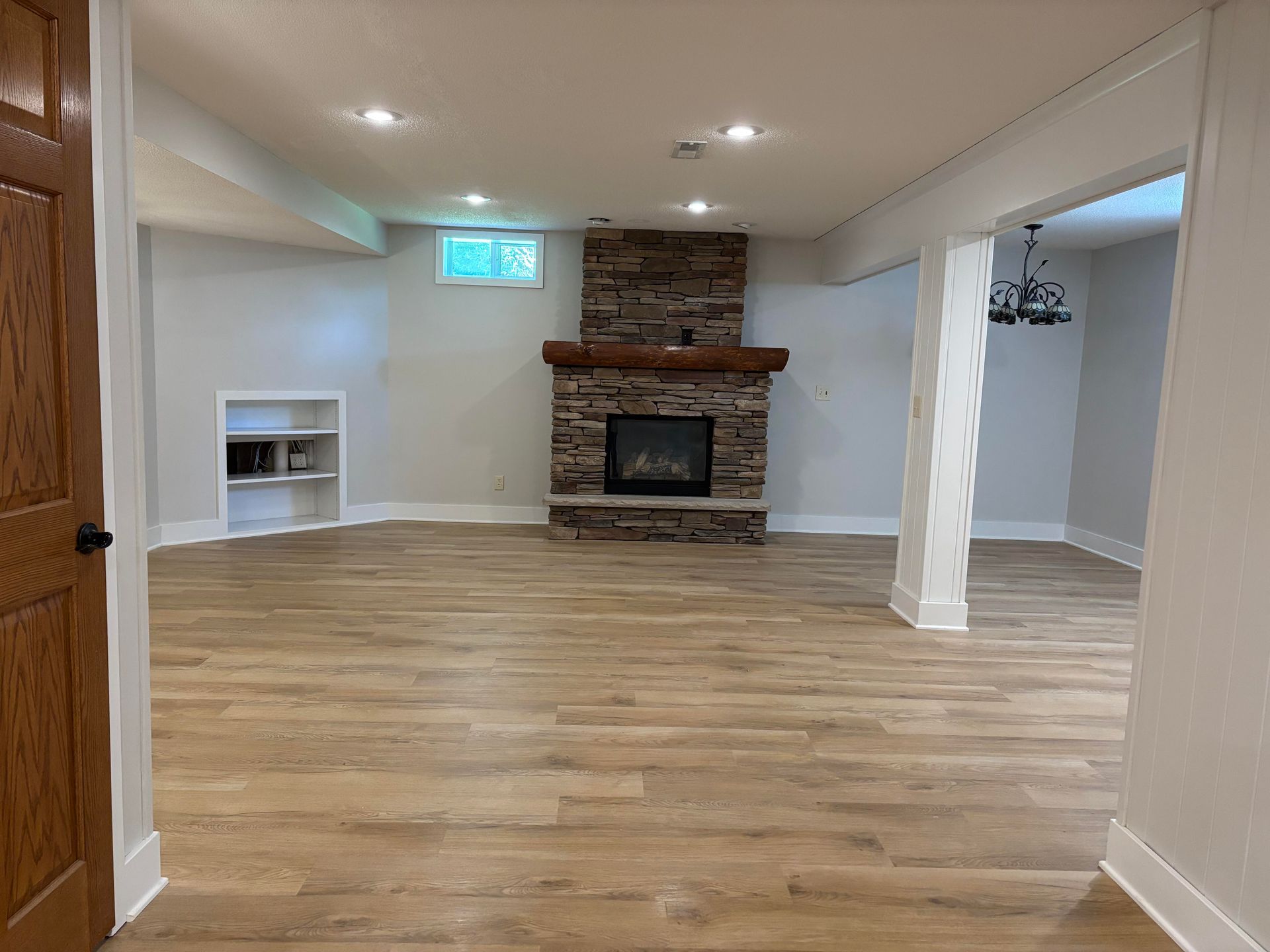 Empty basement with fireplace, wood-look flooring, built-in shelving, and recessed lighting.