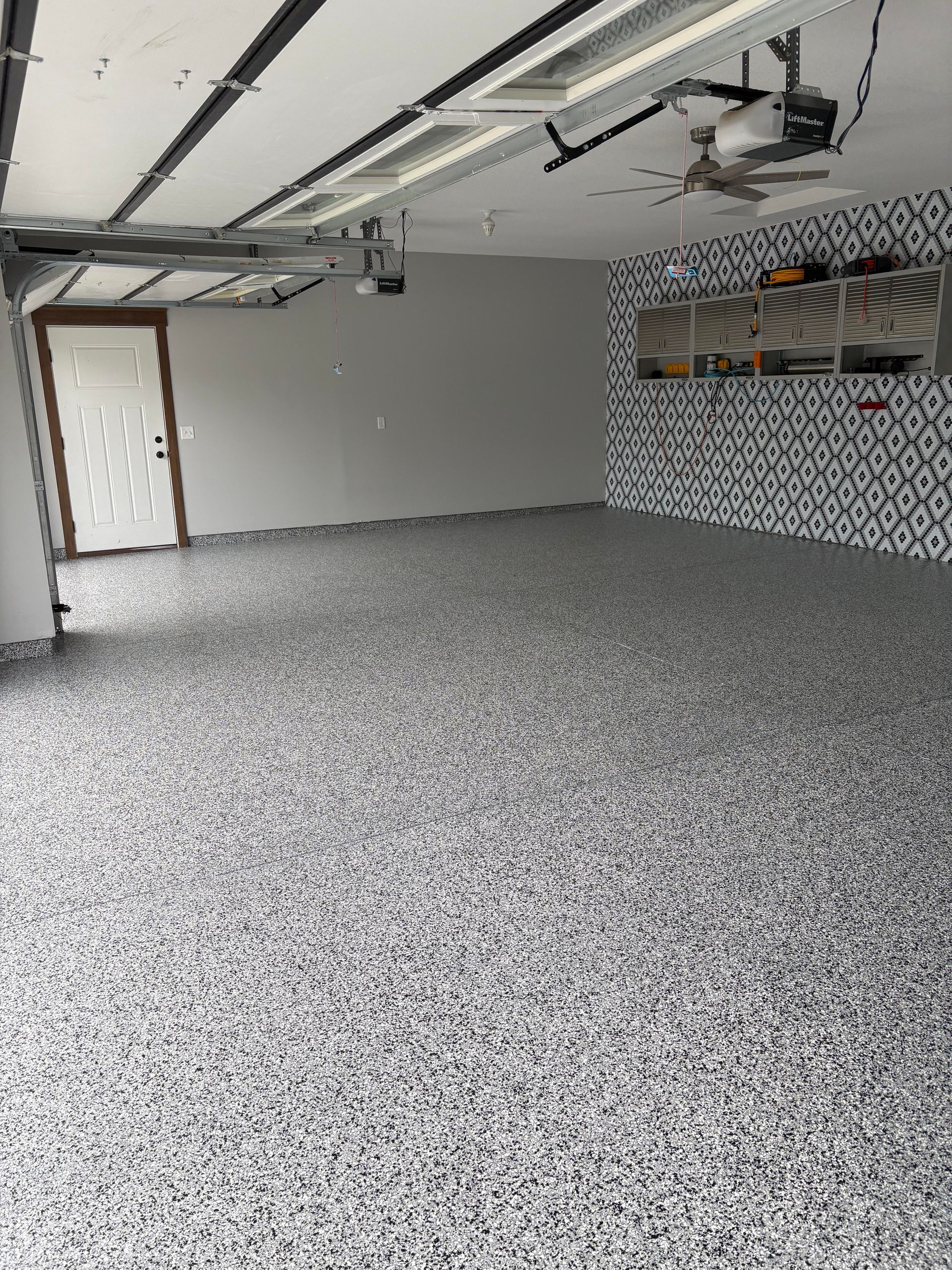 Garage interior with epoxy floor, gray walls, mosaic accent wall, and ceiling mounted door opener.