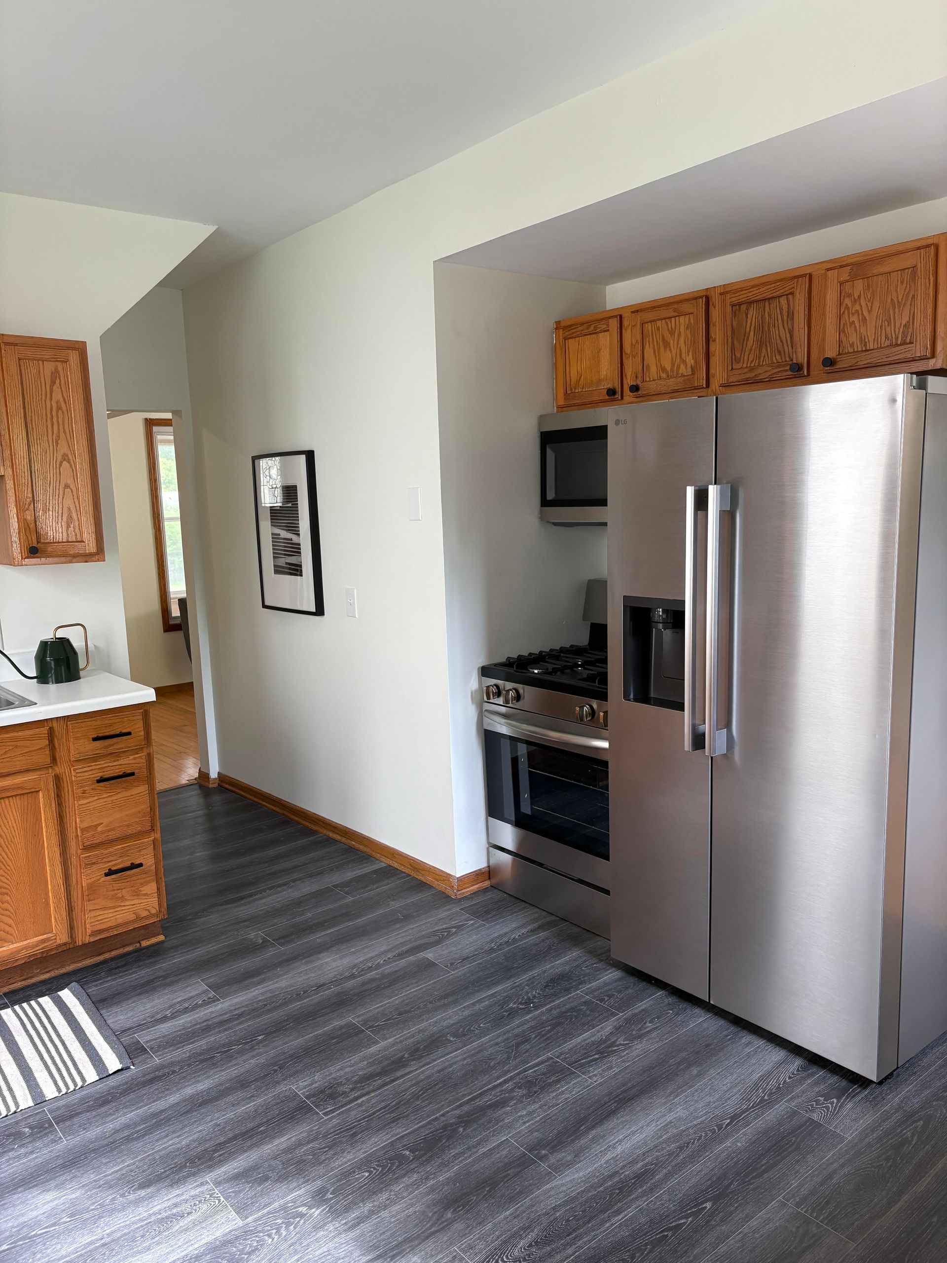 A kitchen with wood cabinets, stainless steel appliances, dark grey flooring, and a cream-colored wall.
