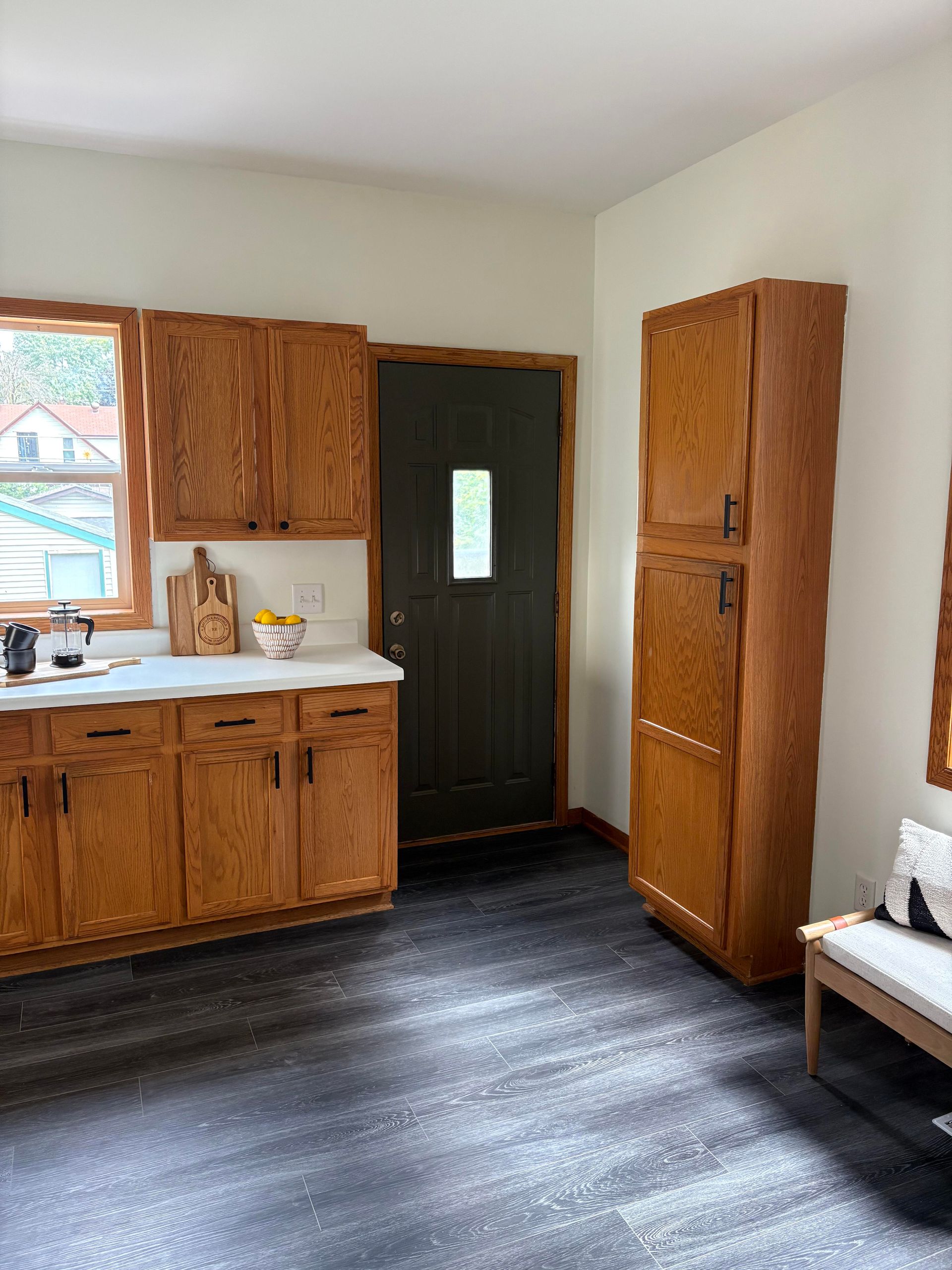 Kitchen with light countertops, wood cabinets, black door, and dark flooring.