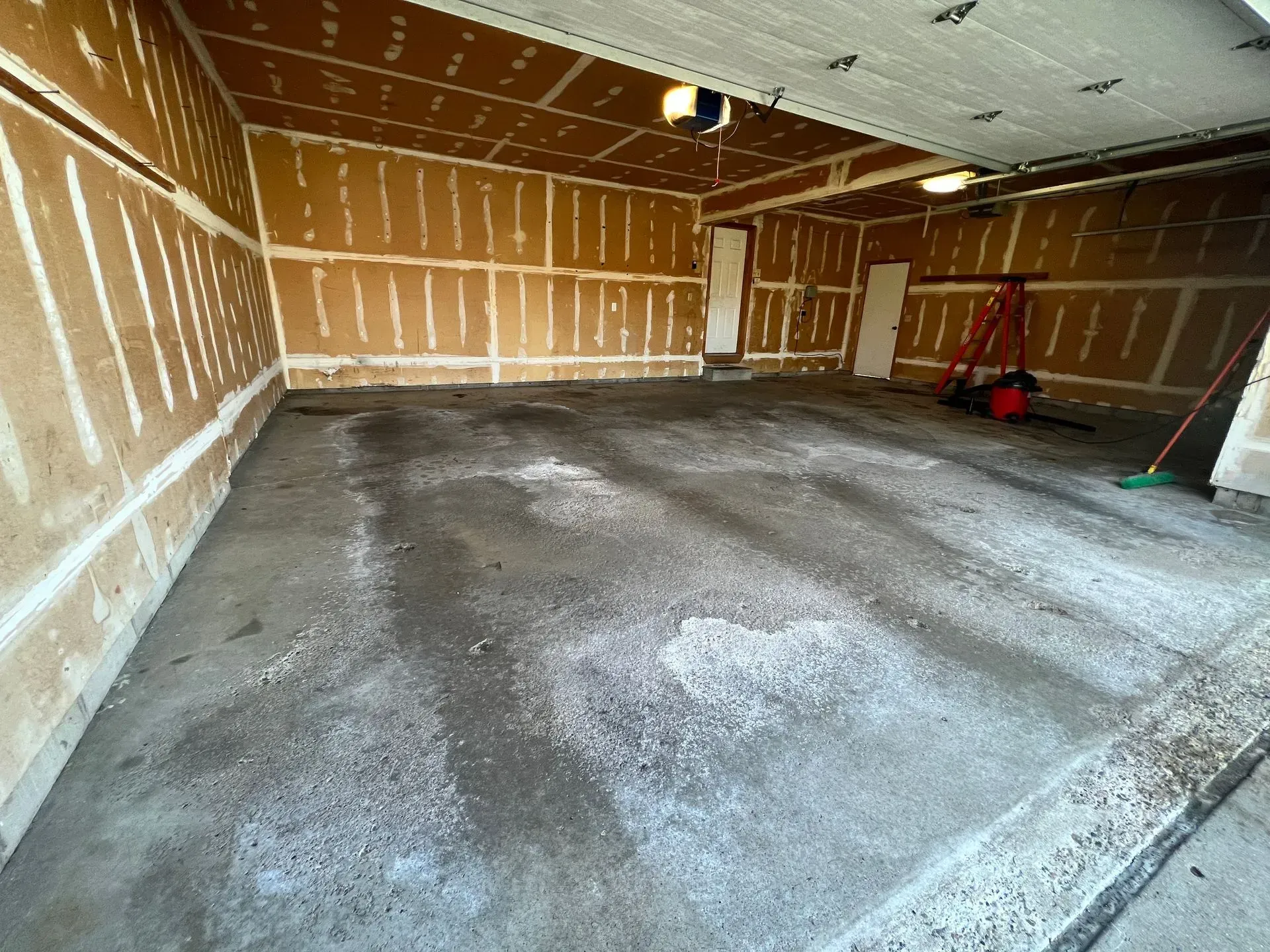 Empty garage interior with concrete floor, drywall walls, and two doors.