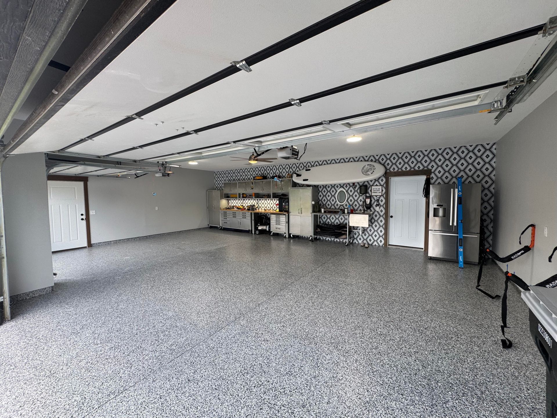 Spacious garage with epoxy floor, organized storage, a decorative accent wall, and a surfboard.