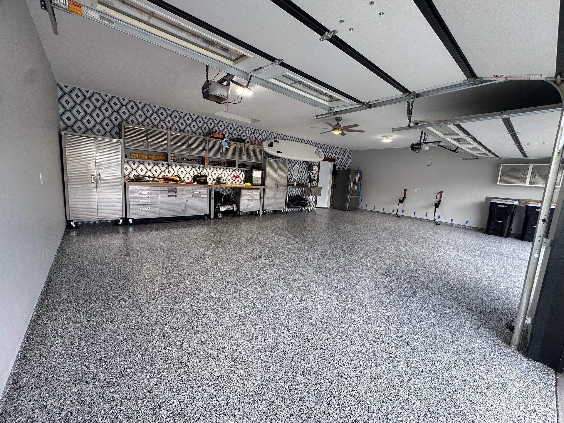 Spacious, well-organized garage with speckled gray flooring, stainless steel cabinets, and patterned accent wall.