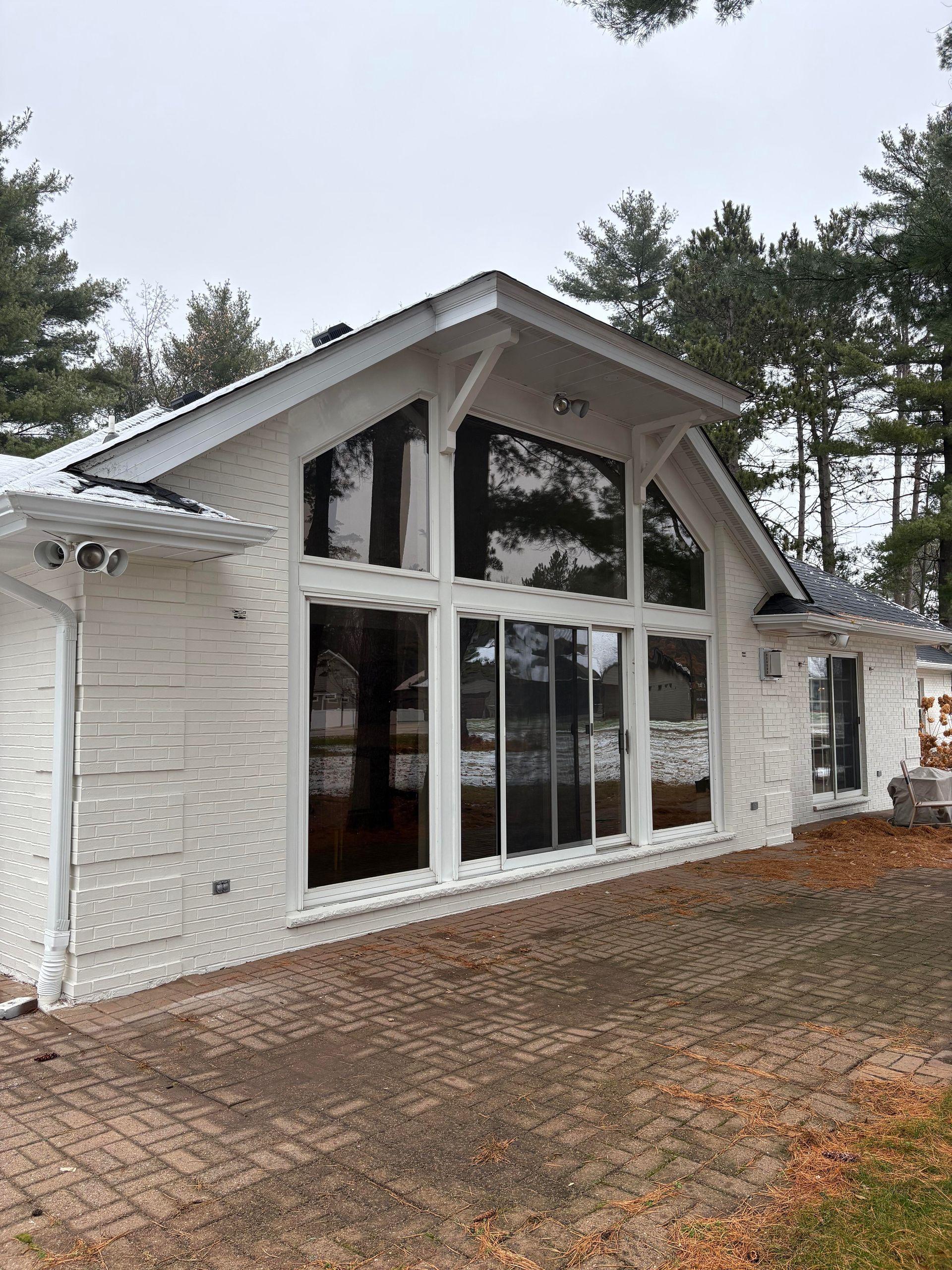 White brick house with large windows, set on a brick patio. Overcast day.