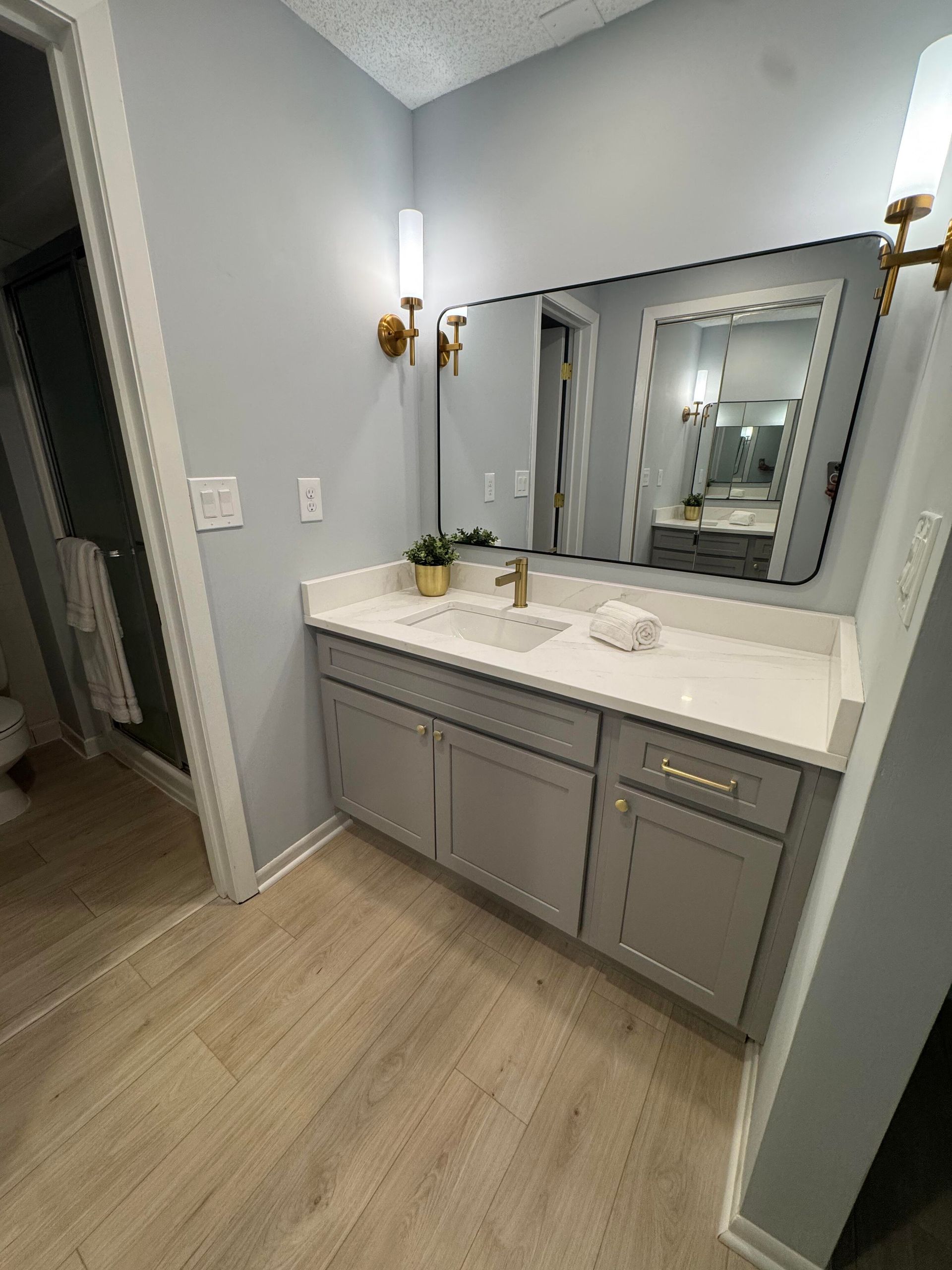 Bathroom with gray vanity, white countertop, gold fixtures, and a large mirror.