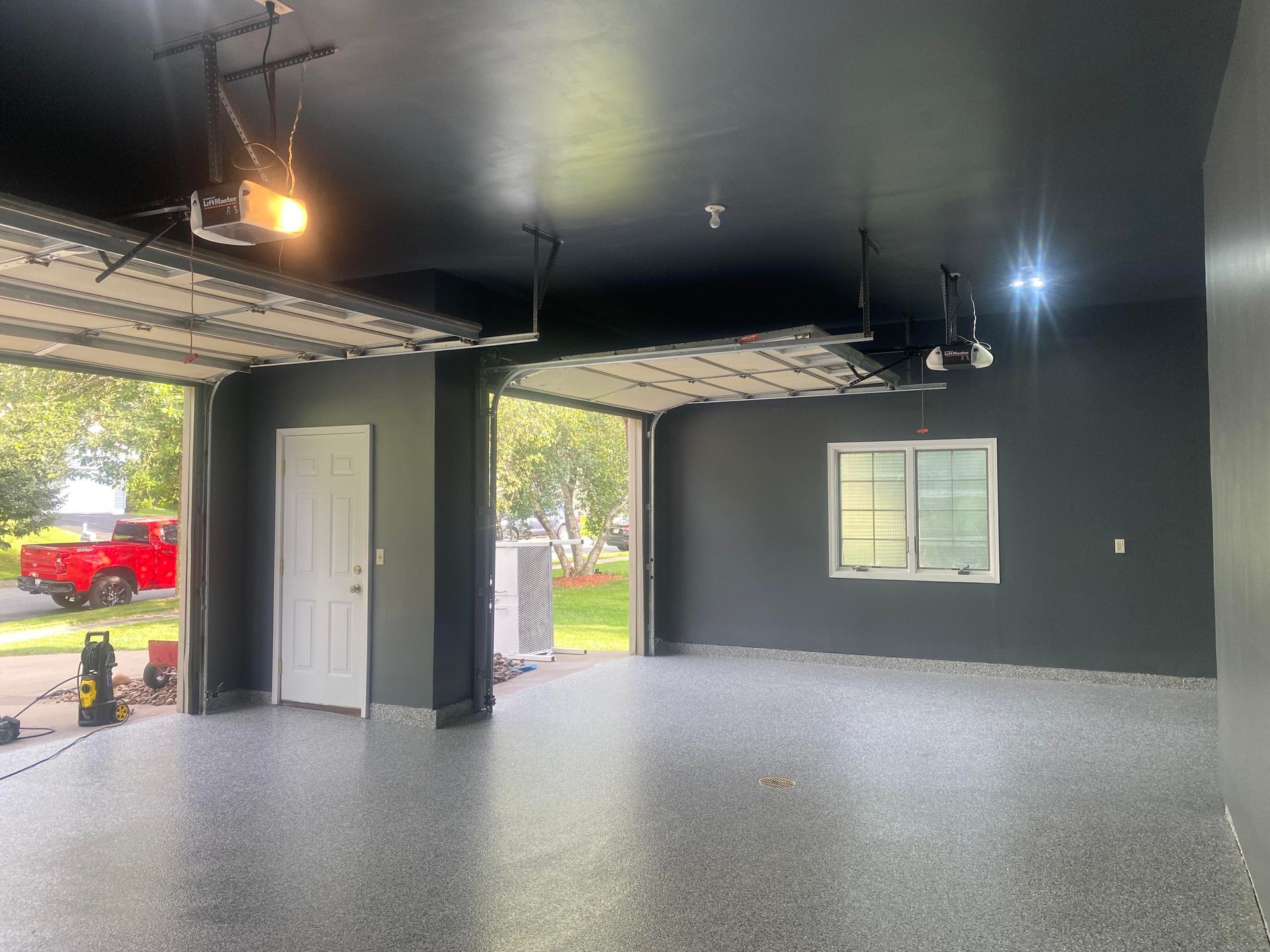 A newly painted garage with a black ceiling and gray walls, two open garage doors, and a red truck visible outside.