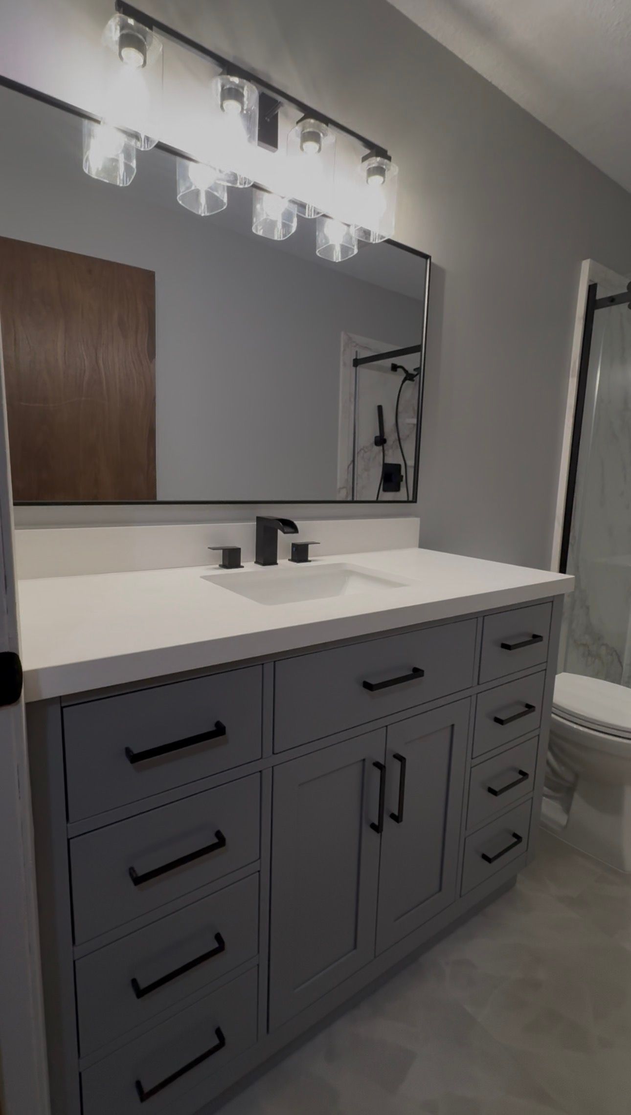 Bathroom with gray vanity, black hardware, white countertop, large mirror, and glass shower.