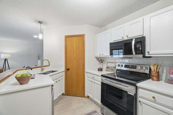 White kitchen with white cabinets, stainless steel appliances, and a wooden door.