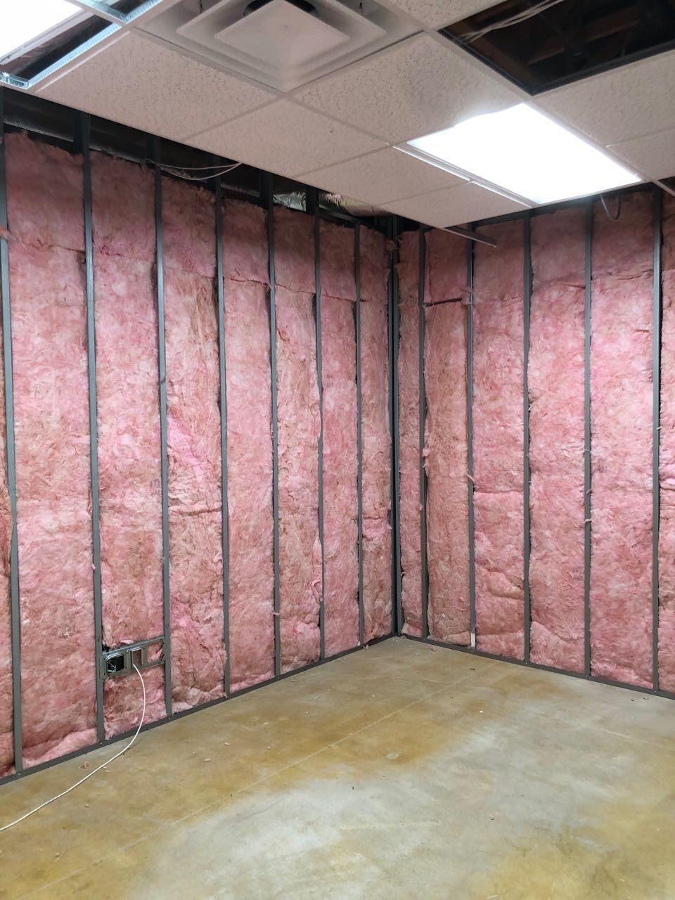 Framing of a room interior with pink insulation between metal studs.